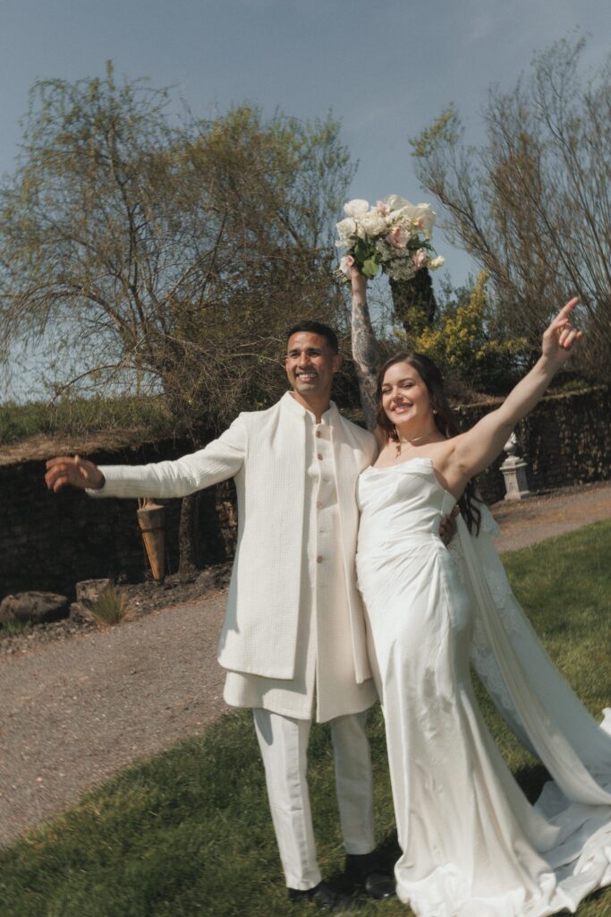 Bride and groom cheering in courtyard surrounded by lush greenery and old-world stone walls