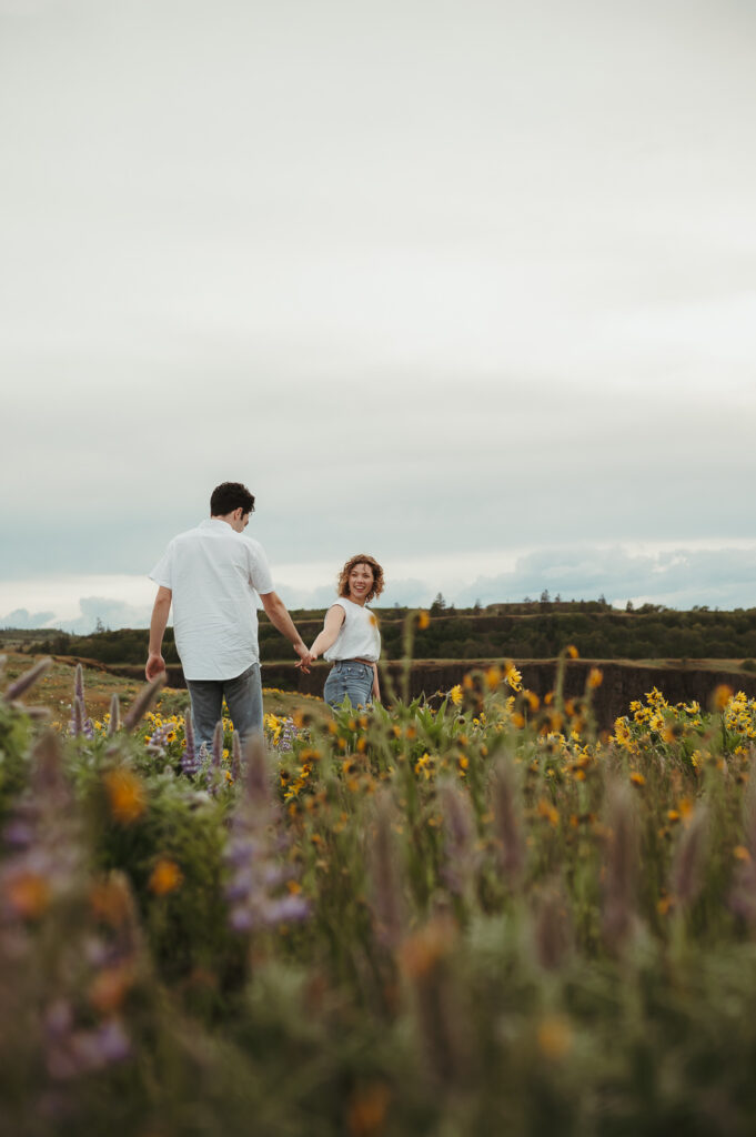 A couple holding hands and walking through wildflowers